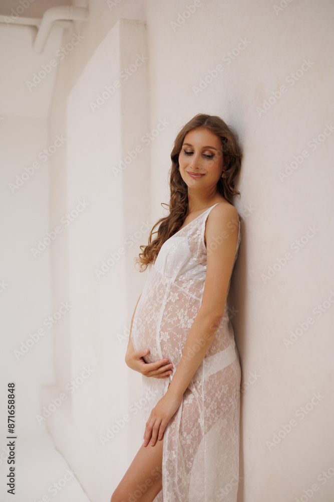 Beautiful pregnant woman in white retro underwear lace dress and white sandals with high heels. Big pregnant belly. Pretty woman waiting child. Light play on woman's body and face Beautiful pregnant woman in white retro underwear lace dress and white sandals with high heels. Big pregnant belly. Pretty woman waiting child. Light play on woman's body and face