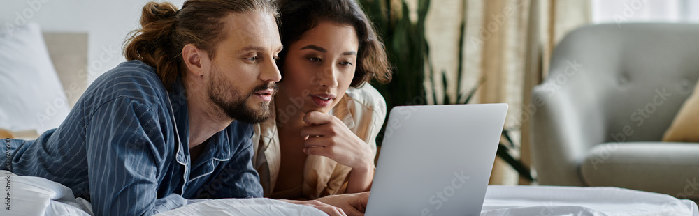 A loving couple cuddles in bed while looking at a laptop. A loving couple cuddles in bed while looking at a laptop.