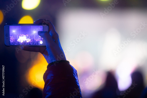 Person holding smartphone with background silhouettes of concert crowd with stage lights