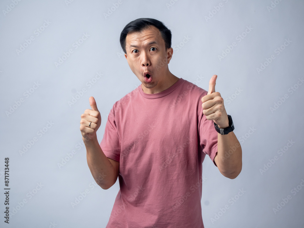 A man in a pink shirt smiles and gives a thumbs-up gesture, exuding positivity and approval. The plain light blue background highlights his cheerful and confident demeanor. A man in a pink shirt smiles and gives a thumbs-up gesture, exuding positivity and approval. The plain light blue background highlights his cheerful and confident demeanor.