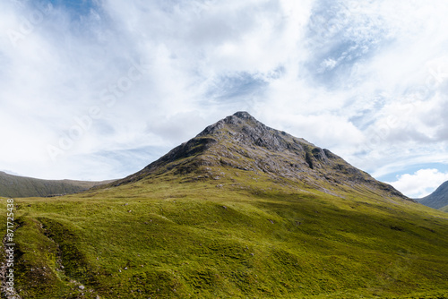 Wide view of Glencoe Valley with a winding river, green mountains, and a bright blue sky filled with fluffy clouds.