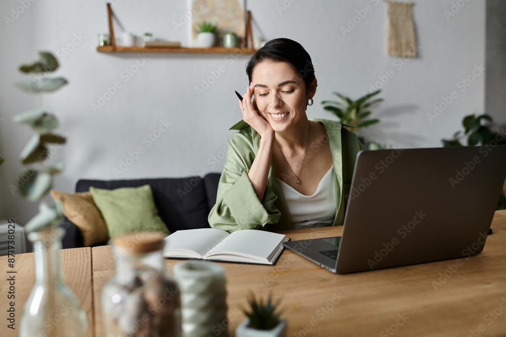 A woman works on her laptop from home, smiling while taking a break to write in a notebook. A woman works on her laptop from home, smiling while taking a break to write in a notebook.