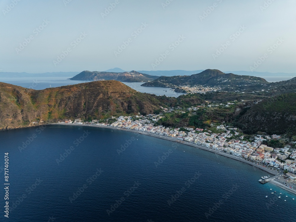 Aerial view of Canneto small town along the Mediterranean coastline with Vulcano Island in background, Lipari, Aeolian Islands archipelagos, Sicily, Italy. Aerial view of Canneto small town along the Mediterranean coastline with Vulcano Island in background, Lipari, Aeolian Islands archipelagos, Sicily, Italy.