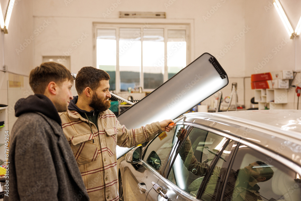 Two men sharing a conversation while gesturing at a car in a garage who have multiple damages at hail