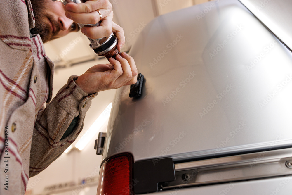Man fixing silver car with hand gestures near vehicle door and bumper