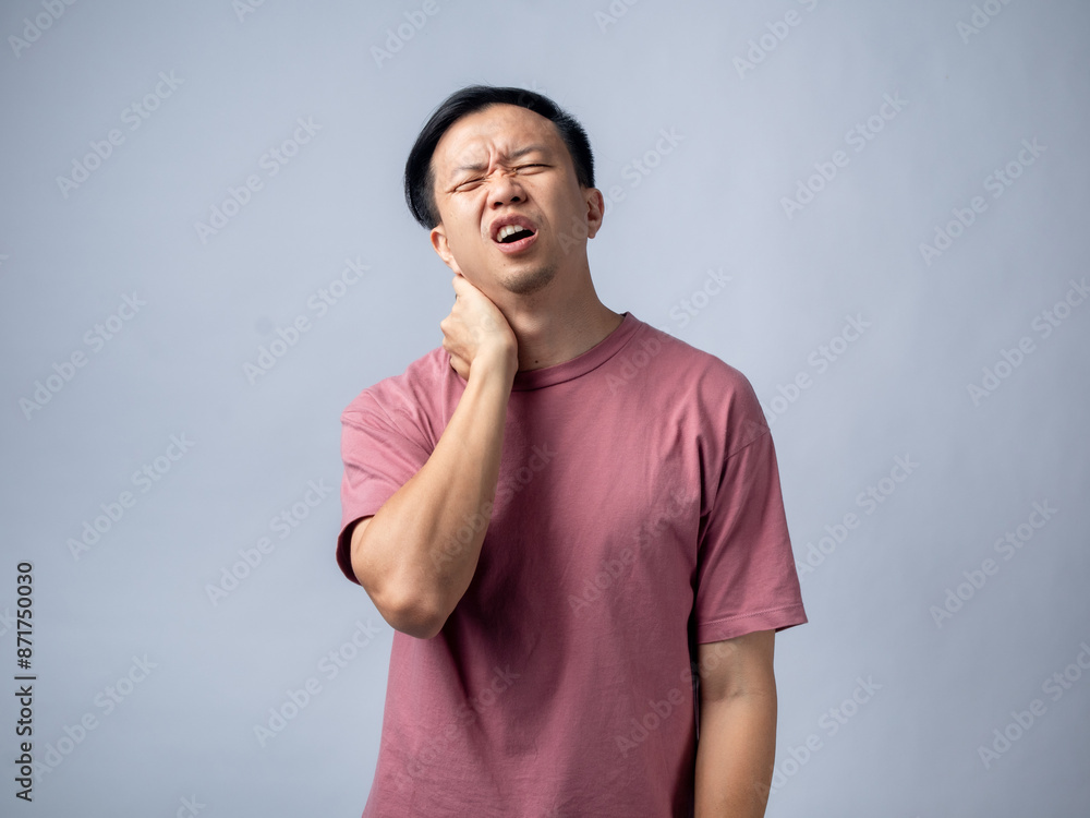 A man in a pink shirt holds his neck with a pained expression, indicating discomfort or neck pain. The plain light blue background emphasizes his distress and highlights A man in a pink shirt holds his neck with a pained expression, indicating discomfort or neck pain. The plain light blue background emphasizes his distress and highlights