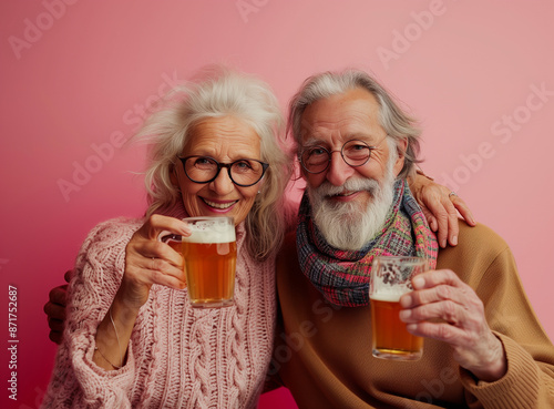 Happy senior couple over pink background holding cups with beers.