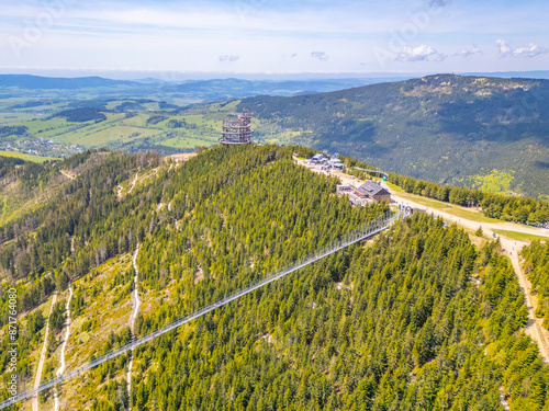 Aerial view of the Sky Bridge 721, the worlds longest suspension footbridge, stretching across a forested mountain in Czechia. The unique Sky Walk lookout tower stands nearby, offering panoramic views photo