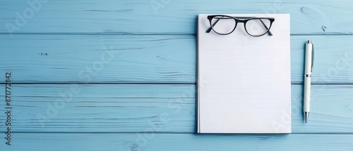 Flat lay of eyeglasses, a blank notepad, and a pen on a blue wooden desk. Perfect for productivity, writing, and planning concepts. photo