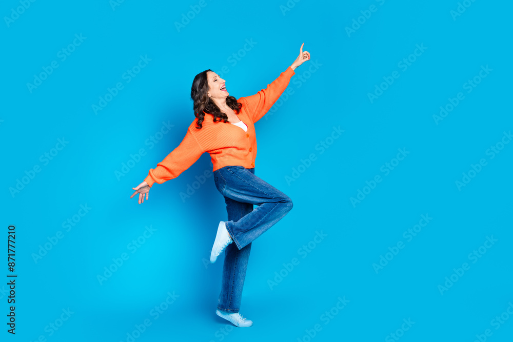 Full body photo of attractive senior woman dancing have fun dressed stylish orange clothes isolated on blue color background Full body photo of attractive senior woman dancing have fun dressed stylish orange clothes isolated on blue color background