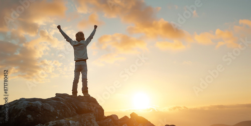 A child boy or kid in silhouette with arms up raised at sunset or sunrise on a mountain top concept