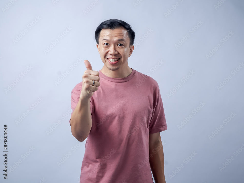 A man in a pink shirt smiles and gives a thumbs-up gesture, exuding positivity and approval. The plain light blue background highlights his cheerful and confident demeanor. A man in a pink shirt smiles and gives a thumbs-up gesture, exuding positivity and approval. The plain light blue background highlights his cheerful and confident demeanor.