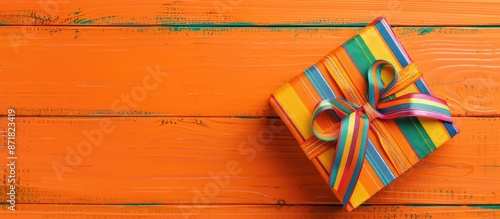 A lovely present box with a colorful ribbon on an orange wooden surface, seen from above with a blank area for your design, embodying a Christmas theme.