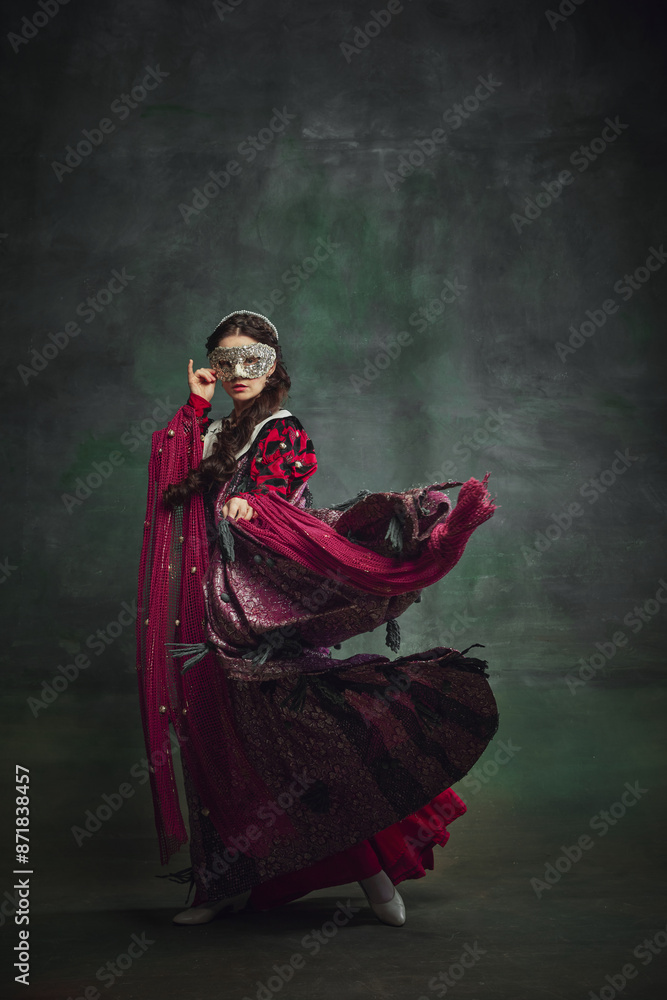 Woman in richly detailed Renaissance-style gown and ornate masks standing against dark green backdrop, exuding mystery and historical elegance. Concept of history, comparison of eras, remake Woman in richly detailed Renaissance-style gown and ornate masks standing against dark green backdrop, exuding mystery and historical elegance. Concept of history, comparison of eras, remake