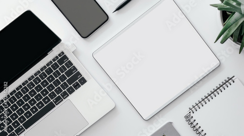 A white notebook sits open next to a Macbook Pro. The Macbook Pro has a blank white screen. The devices are on a white background in Batumi, Georgia. (April 10, 2023)