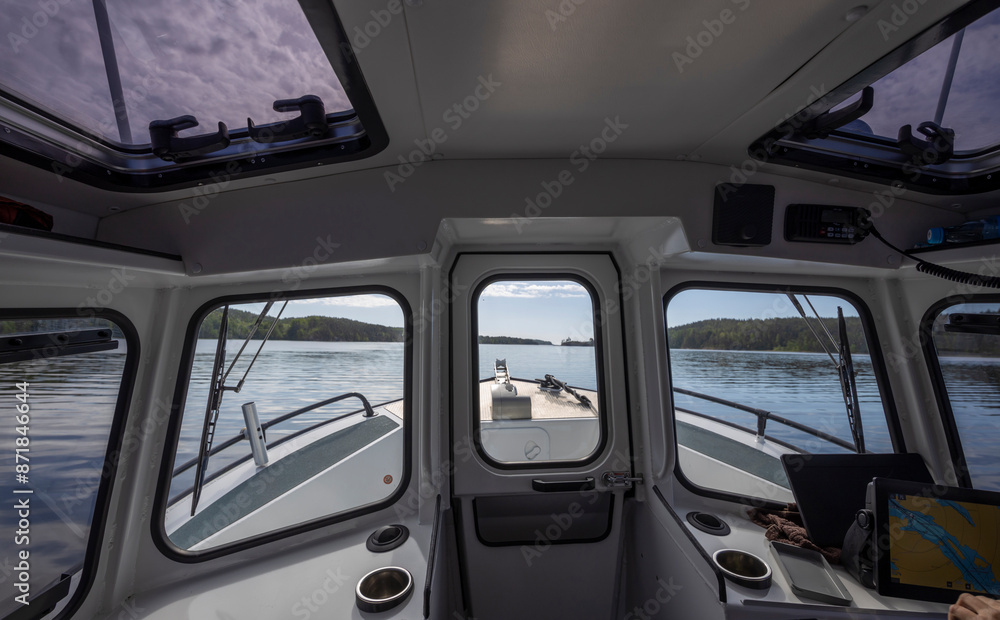 A view from the helm of a boat, with the bow visible through a large window. The calm waters and distant shoreline offer a peaceful seascape. A view from the helm of a boat, with the bow visible through a large window. The calm waters and distant shoreline offer a peaceful seascape.