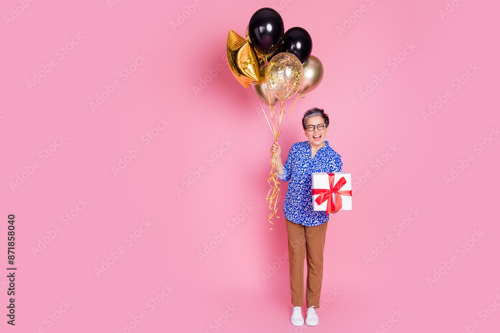 Full size photo of funky person dressed print blouse pants holding balloons gift near empty space isolated on pink color background Full size photo of funky person dressed print blouse pants holding balloons gift near empty space isolated on pink color background