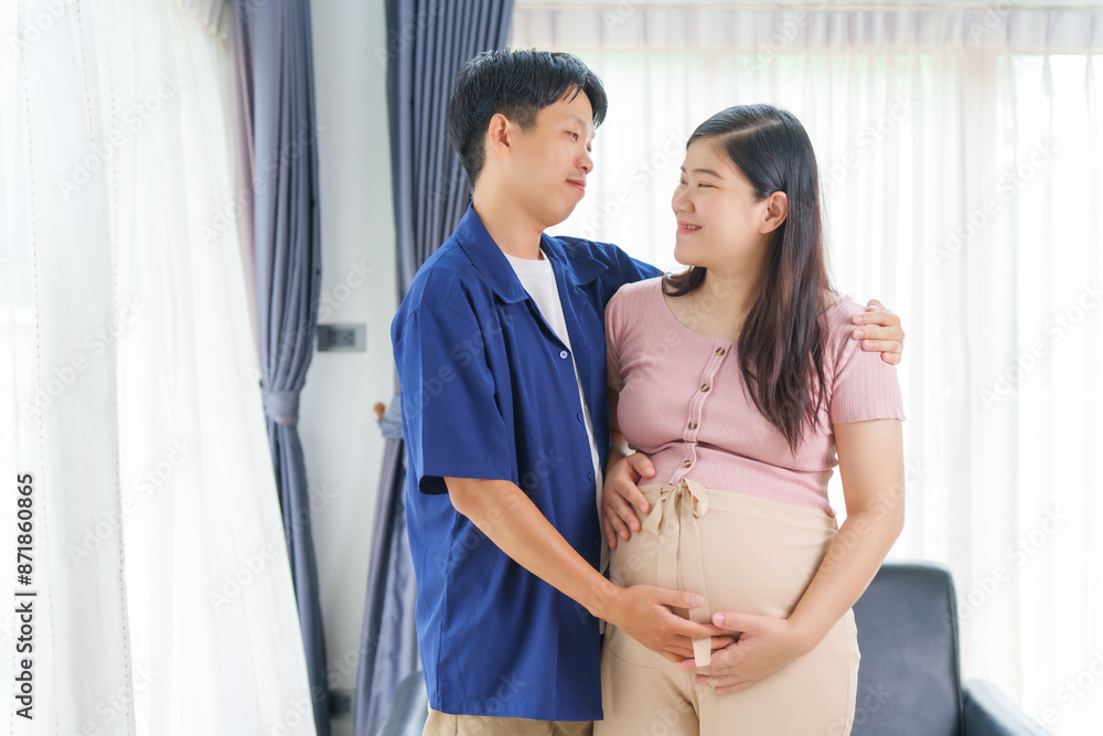 Naklejka premium An Asian young husband gently embraces his pregnant wife at home, their love evident as they prepare for parenthood, cherishing the tender moments of expecting their first child together.