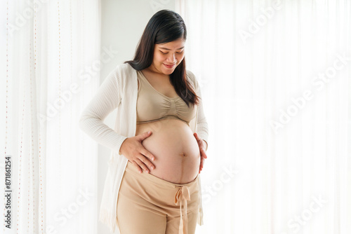 An Asian young pregnant wife relaxes at home, her hand gently resting on her belly, filled with love and anticipation as she embraces the journey of impending motherhood. Free Download An Asian young pregnant wife relaxes at home, her hand gently resting on her belly, filled with love and anticipation as she embraces the journey of impending motherhood. - GFXLoad