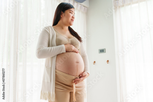 An Asian young pregnant wife relaxes at home, her hand gently resting on her belly, filled with love and anticipation as she embraces the journey of impending motherhood. Free Download An Asian young pregnant wife relaxes at home, her hand gently resting on her belly, filled with love and anticipation as she embraces the journey of impending motherhood. - GFXLoad