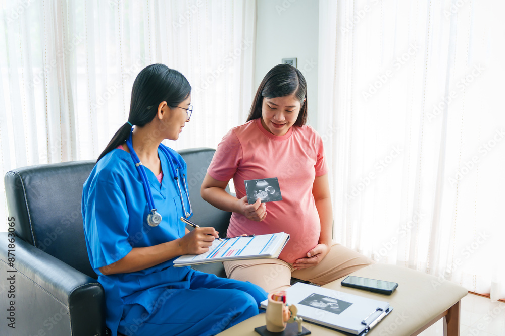Asian female doctor and nurse consult with a pregnant woman on a sofa, using an ultrasound and stethoscope, preparing her for birth ahead of schedule with care and expertise. Asian female doctor and nurse consult with a pregnant woman on a sofa, using an ultrasound and stethoscope, preparing her for birth ahead of schedule with care and expertise.