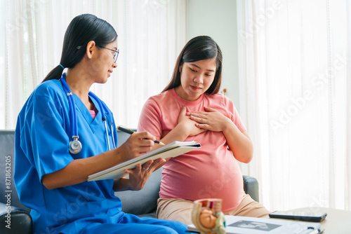 Asian female doctor and nurse consult on sofa with a pregnant woman, using ultrasound and stethoscope, addressing illnesses morning sickness, gestational diabetes, hypertension, ensuring her health. photo