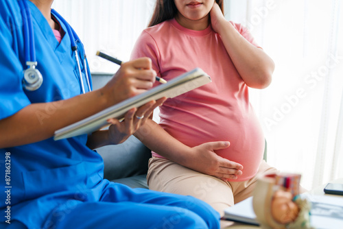 Asian female doctor and nurse consult on sofa with a pregnant woman, using ultrasound and stethoscope, addressing illnesses morning sickness, gestational diabetes, hypertension, ensuring her health. photo