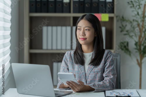 Sharing good business news. Attractive young businesswoman talking on the mobile phone and smiling while sitting at her working place in office and looking at laptop PC.