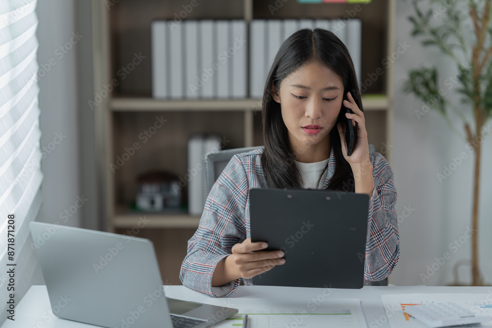 Sharing good business news. Attractive young businesswoman talking on the mobile phone and smiling while sitting at her working place in office and looking at laptop PC. Sharing good business news. Attractive young businesswoman talking on the mobile phone and smiling while sitting at her working place in office and looking at laptop PC.