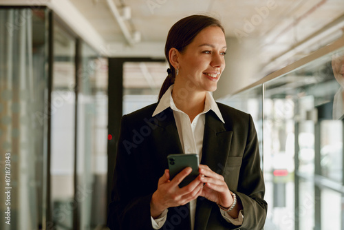 A confident businesswoman in professional attire is using a smartphone in a modern office setting photo
