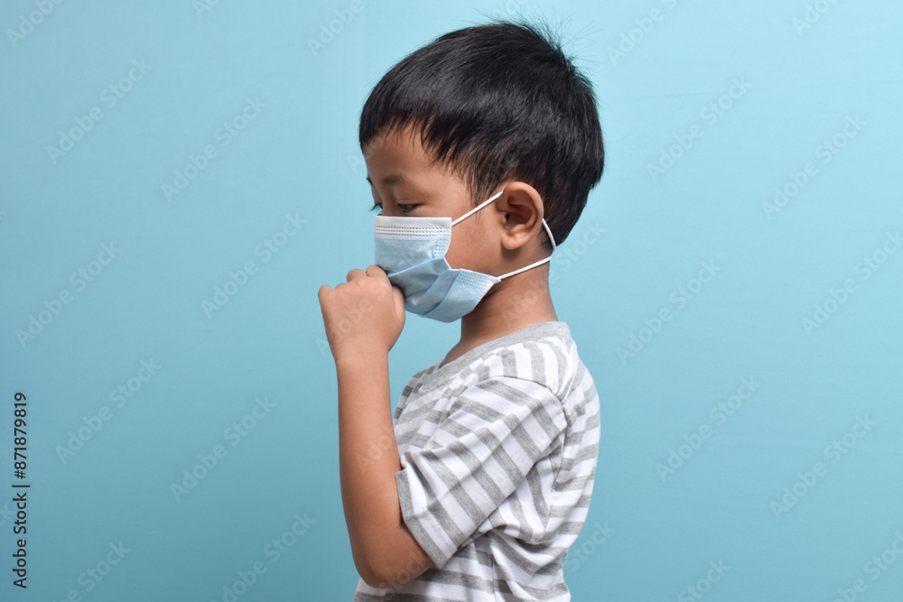 Side portrait of Asian Boy wearing health mask isolated on blue background. Cute little boy holding mask and coughing. Medical and health concept Side portrait of Asian Boy wearing health mask isolated on blue background. Cute little boy holding mask and coughing. Medical and health concept