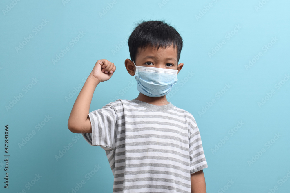 Asian Boy wearing health mask isolated on blue background. Confident kid shows his biceps arm muscle. Medical and health concept