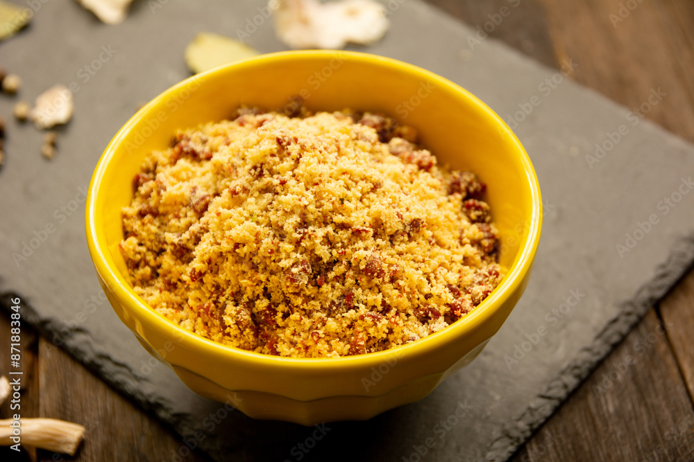Brazilian manioc flour farofa with bacon in a yellow bowl Brazilian manioc flour farofa with bacon in a yellow bowl