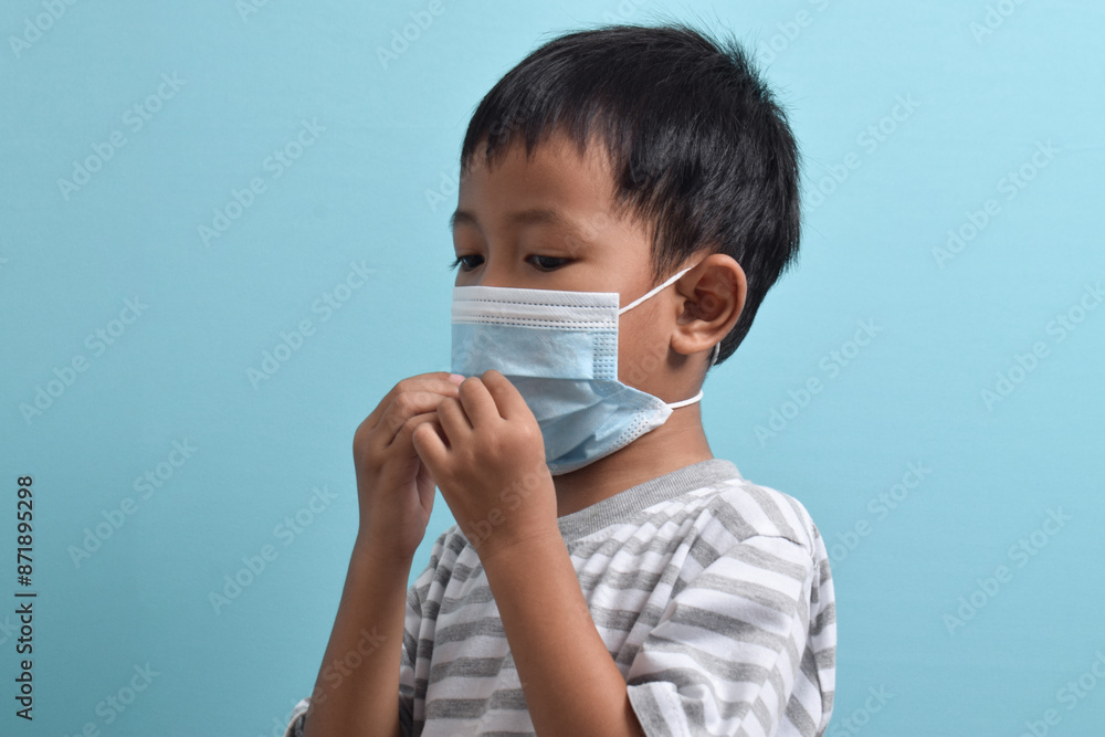 Asian Boy wearing health mask isolated on blue background. Medical and health concept. Human population viruses, infections, flu disease prevention Asian Boy wearing health mask isolated on blue background. Medical and health concept. Human population viruses, infections, flu disease prevention