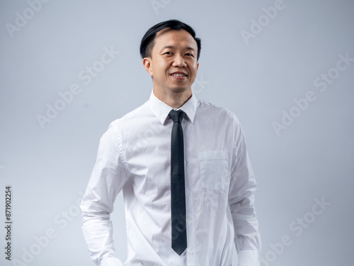 Asian businessman in a white shirt and black tie smiling confidently, standing sideways against a plain light background. The image portrays confidence, professionalism, and success