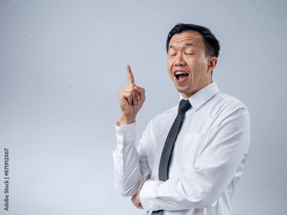 Asian businessman in a white shirt and black tie raising his index finger as if sharing an idea, looking up with an excited expression against a plain light background. The image conveys innovation Asian businessman in a white shirt and black tie raising his index finger as if sharing an idea, looking up with an excited expression against a plain light background. The image conveys innovation