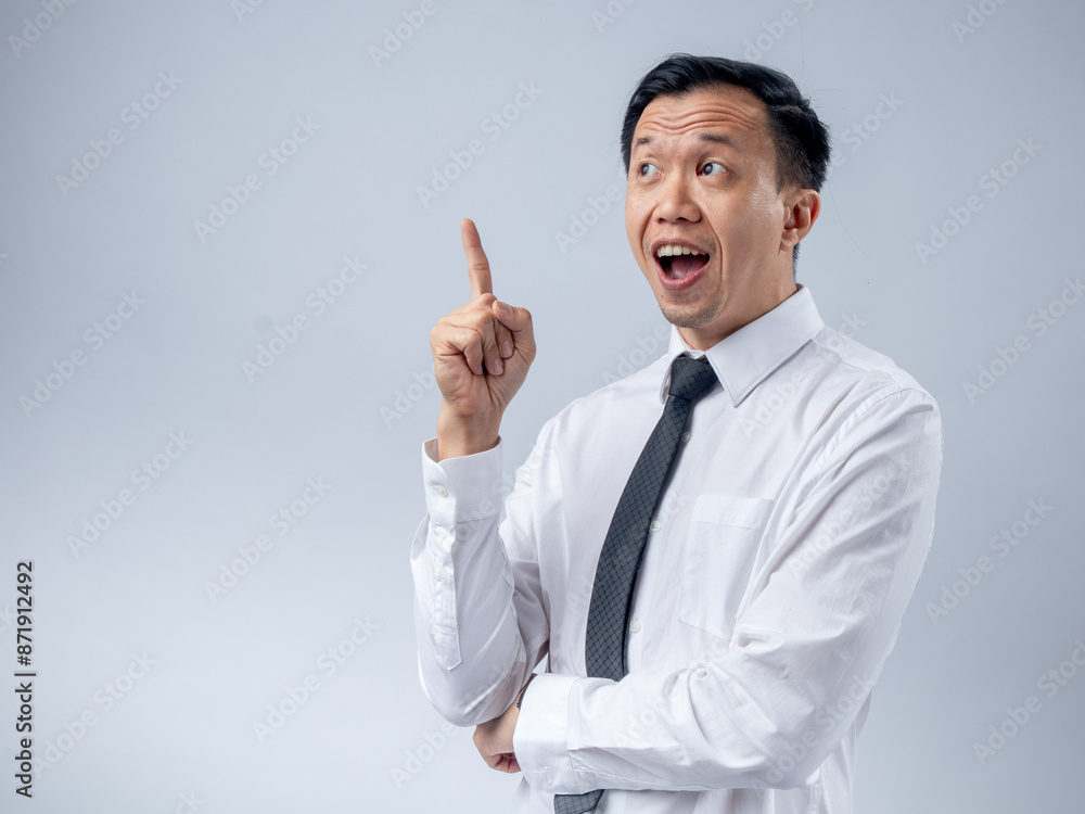 Asian businessman in a white shirt and black tie raising his index finger as if sharing an idea, looking up with an excited expression against a plain light background. The image conveys innovation Asian businessman in a white shirt and black tie raising his index finger as if sharing an idea, looking up with an excited expression against a plain light background. The image conveys innovation