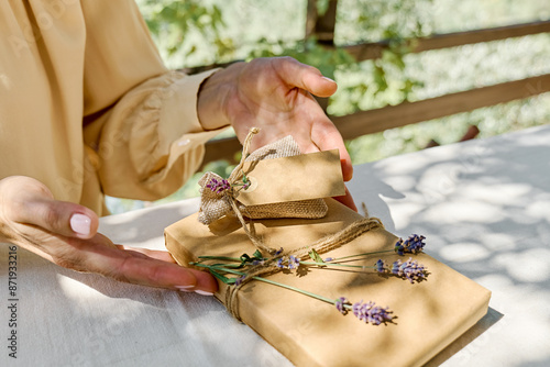 Woman making hand made gift package with craft recycled paper and dried lavender flowers on the table with linen tablecloth. Natural aesthetic. photo