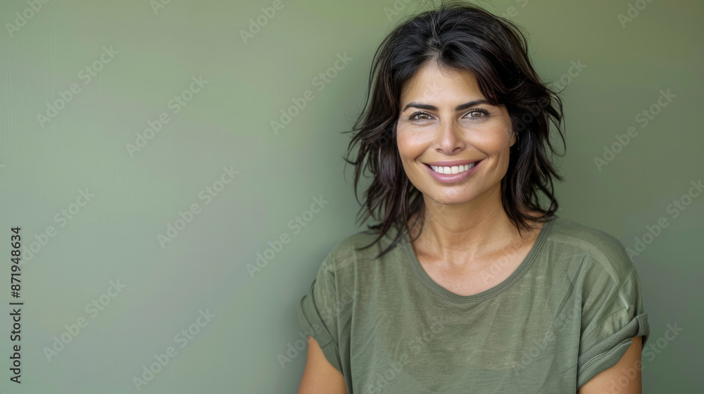 Fototapeta premium Playful and relaxed woman with tousled dark hair and an engaging smile in a green shirt, against a soft green background