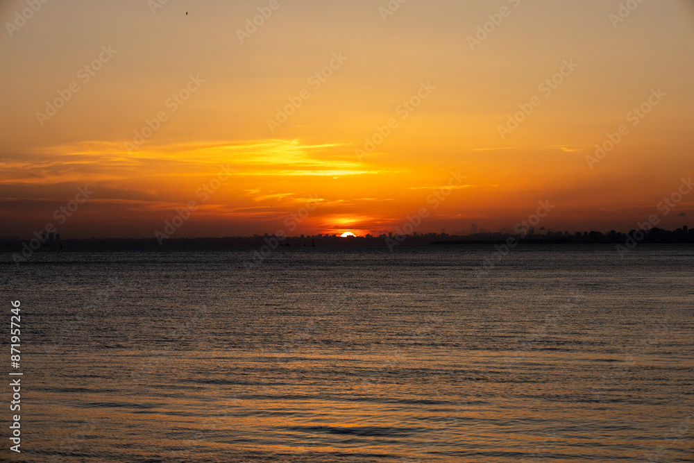 Fototapeta premium Stunning Sunset Over the Calm Waters with a City Skyline in the Distance