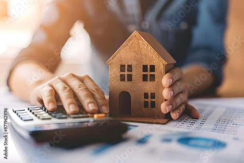 Person using a calculator and holding a small wooden house model, representing mortgage planning or home investment analysis. photo