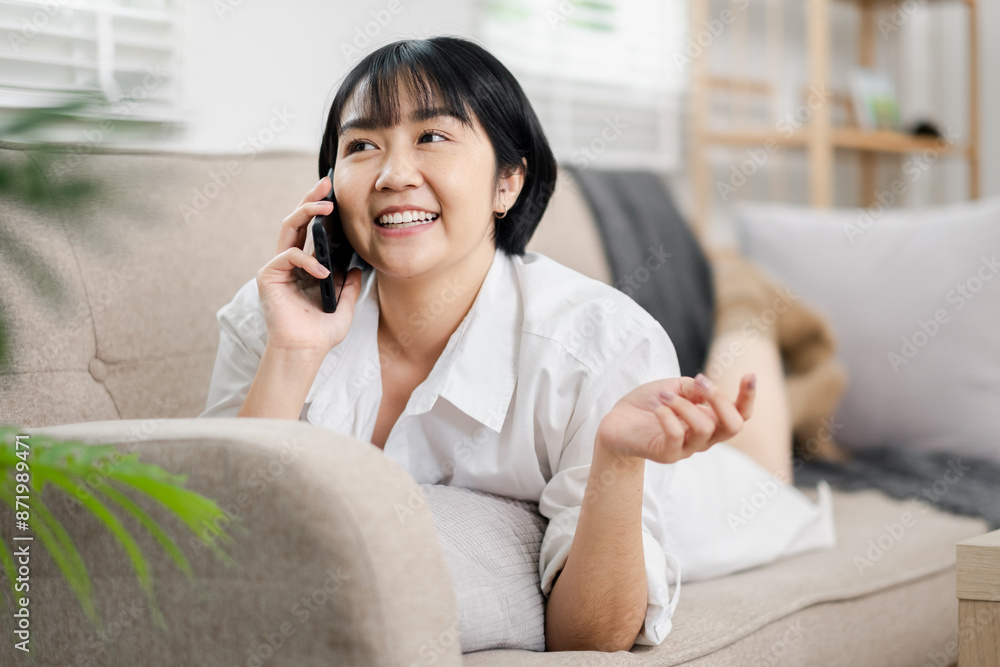 Happy woman lying on couch, chatting on mobile phone in cozy, well-lit living room. Happy woman lying on couch, chatting on mobile phone in cozy, well-lit living room.
