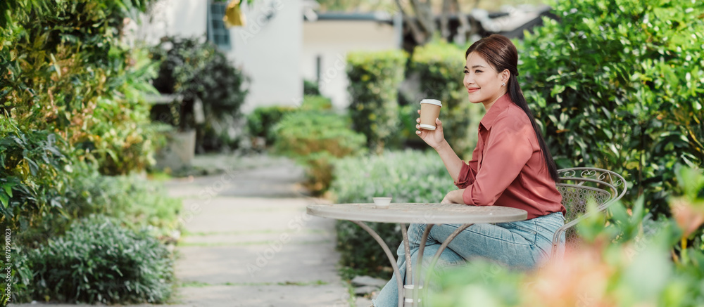 A woman sitting at a table in a garden, holding a coffee cup, surrounded by lush greenery and a pathway. A woman sitting at a table in a garden, holding a coffee cup, surrounded by lush greenery and a pathway.
