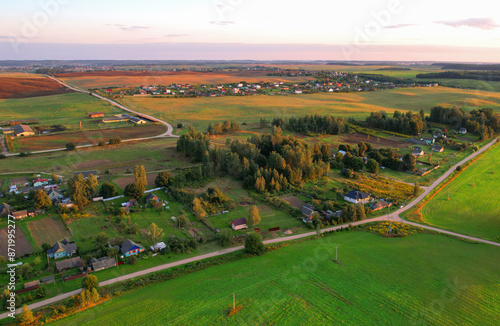 Rural landscape on sunset. Houses in village at green field. Village wooden house in rural. Roofs of Country houses in countryside, drone view. Suburb house at farm field. Countryside, aerial view.