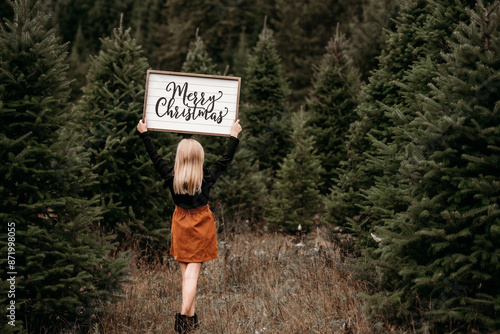 girl holding christmas sign at tree farm photo