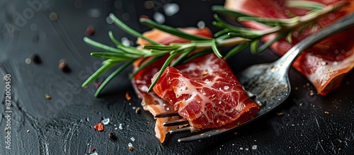 Closeup view of a fork with a delicious slice of jamon and rosemary on a black backdrop, providing space for a copy image. photo