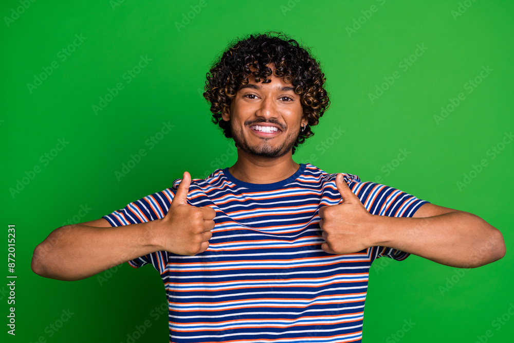 Photo of cheerful glad man wear trendy striped clothes showing thumb up isolated on green color background Photo of cheerful glad man wear trendy striped clothes showing thumb up isolated on green color background