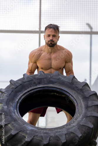 Strong shirtless man doing crossfit with a truck wheel.