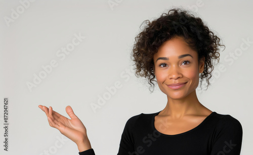 A beautiful, smiling mixed-race woman in a black top extends her open hand, palm up, presenting a blank space for your message or product.