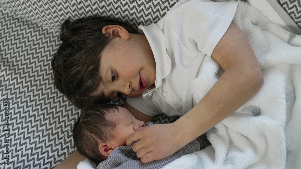 Young boy lovingly touches his newborn sibling's face as they lay side by side, both wrapped in a soft blanket, showcasing the protective and tender bond between brothers Young boy lovingly touches his newborn sibling's face as they lay side by side, both wrapped in a soft blanket, showcasing the protective and tender bond between brothers